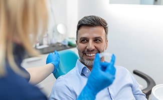 Man smiling at dental assistant holding clear aligner