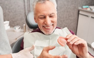 Man smiling while holding mold of dentures