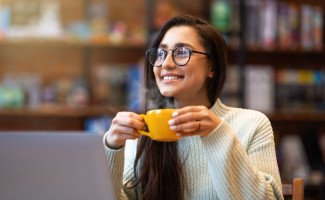 Woman smiling while drinking coffee and working on computer