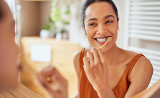Woman smiling while brushing her teeth at home