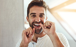 Man smiling while flossing his teeth in bathroom